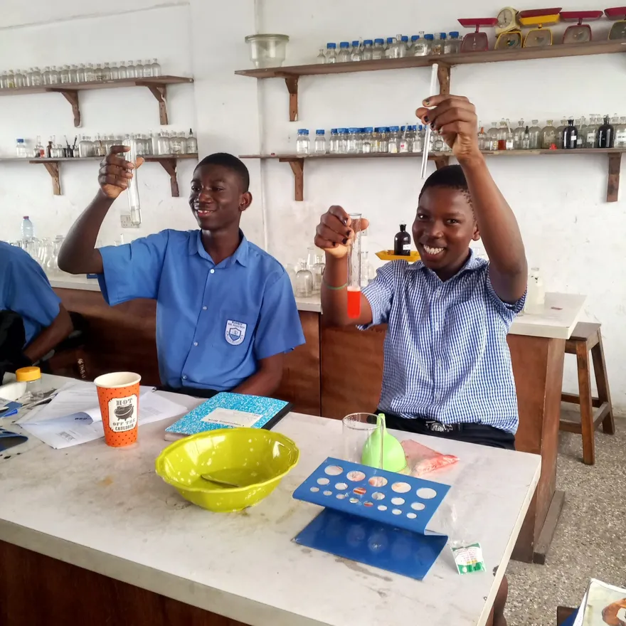 Two Sankofa STEM fellows smiling and holding up their test tubes in a school laboratory