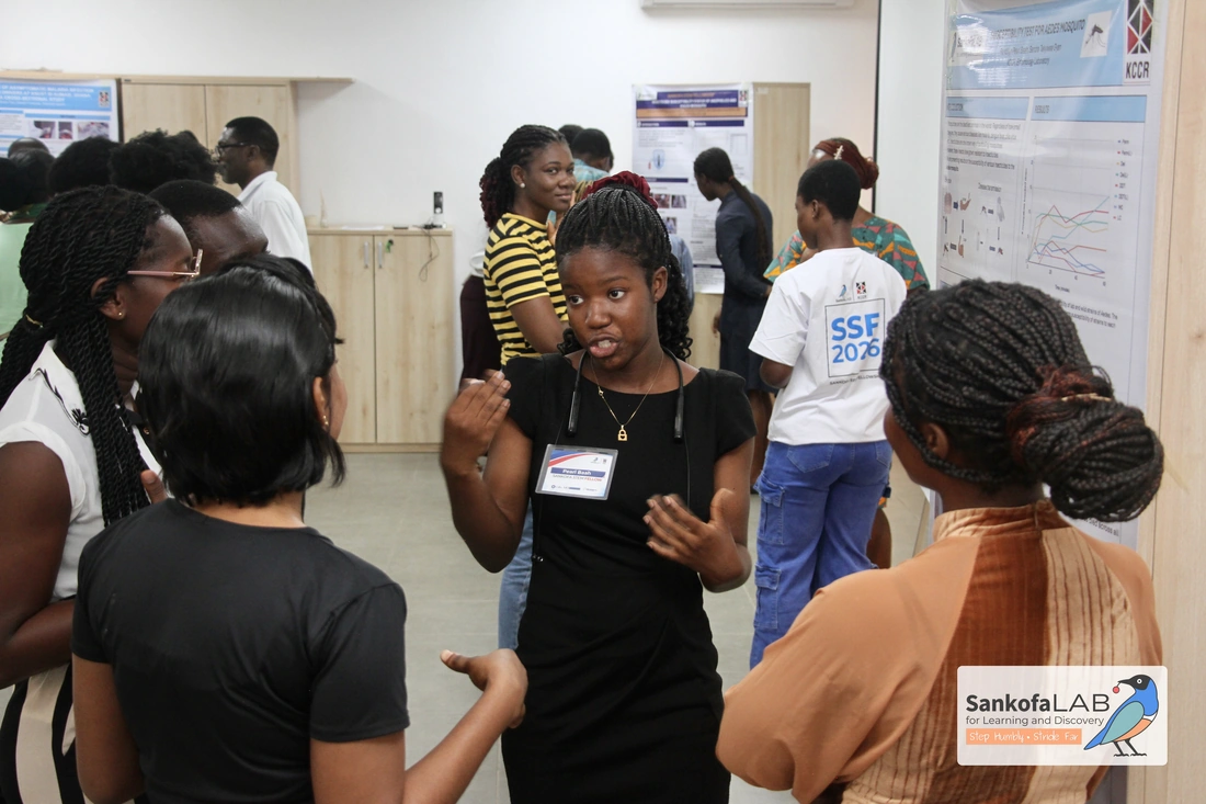 A fellow gestures while explaining a research poster to a small group standing in front of a row of posters